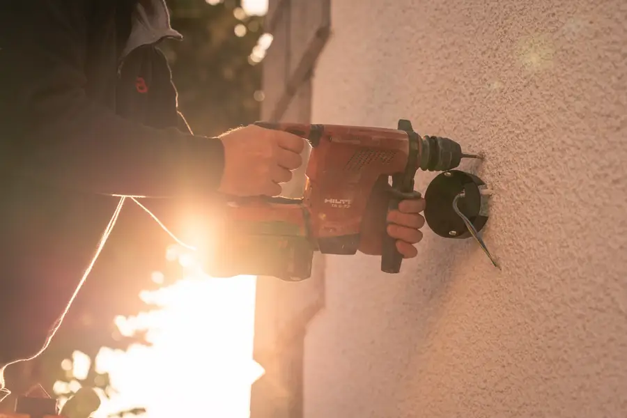 Ouvrier perçant un mur extérieur pour installer un luminaire au coucher du soleil — Lucas Gouritin