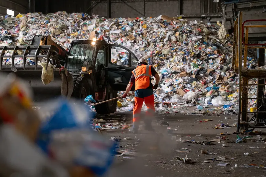 Employé nettoyant une usine de recyclage avec un tas d'ordures en arrière-plan — Lucas Gouritin