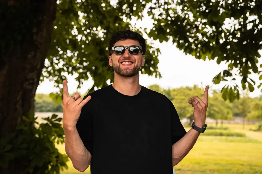 Homme souriant en lunettes de soleil faisant un signe rock en extérieur — Lucas Gouritin